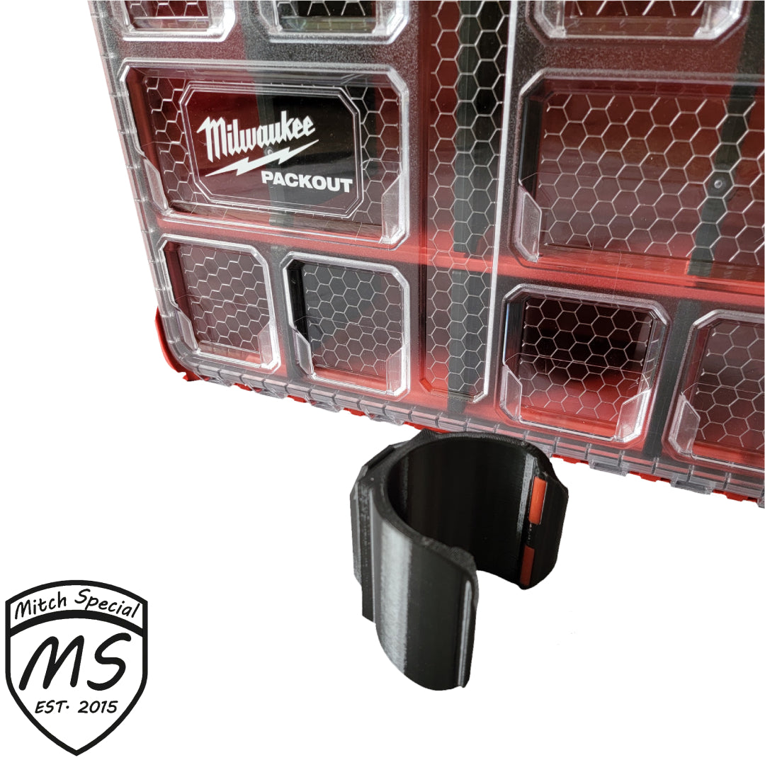 A black holder attachment designed for Milwaukee Packout storage systems, shown attached to a clear and red Packout case.