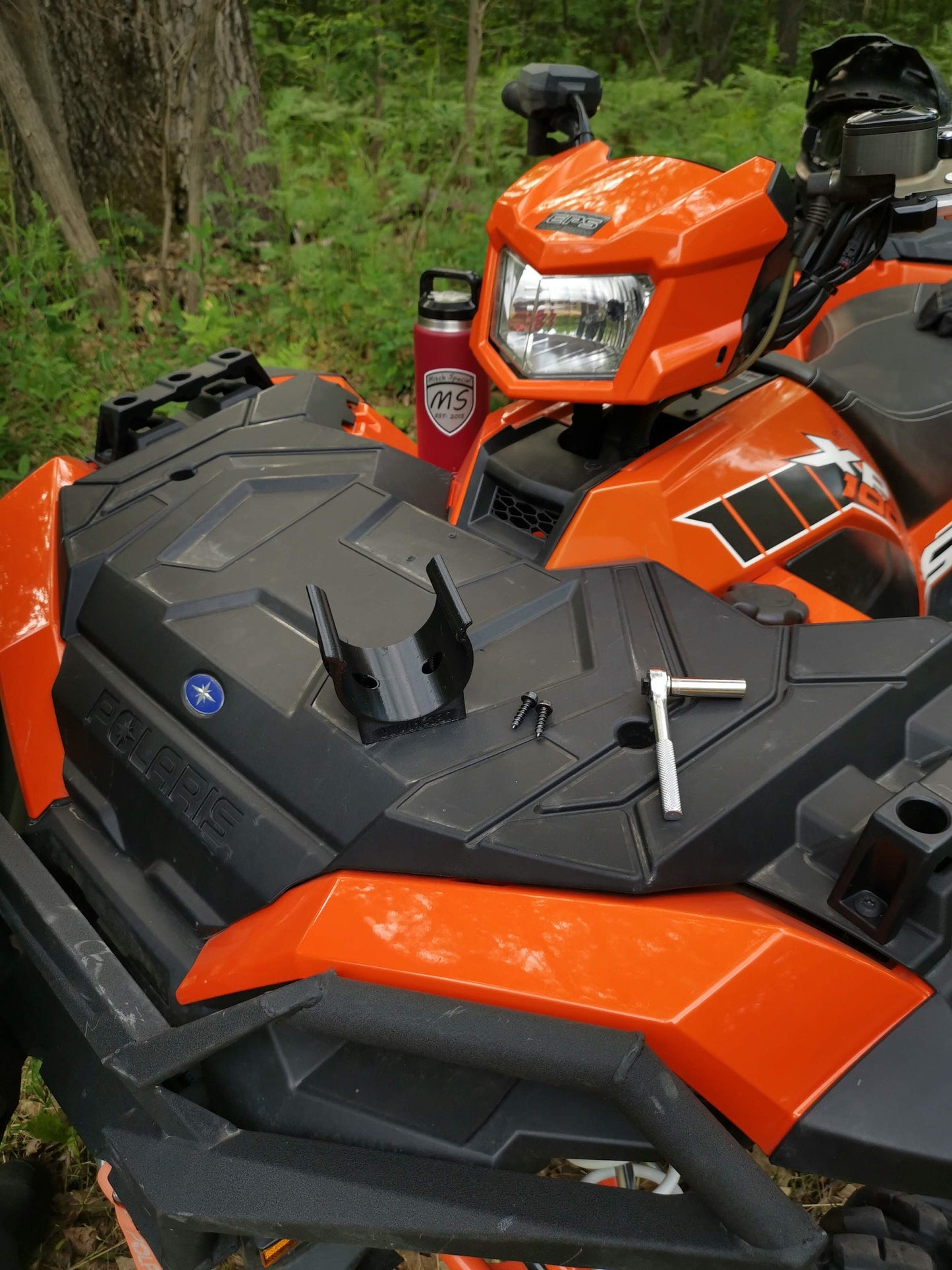 A universal holder designed to mount using two screws is shown on the front of an orange Polaris ATV's front cargo area.
