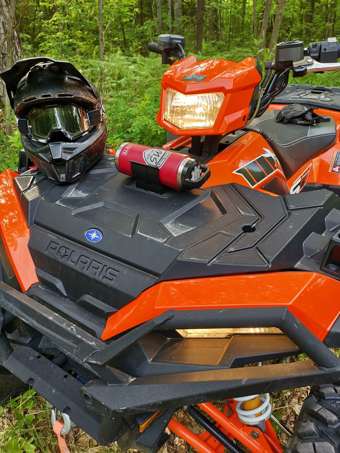 A black helmet and a red fire extinguisher mounted on the front of an orange Polaris ATV, secured using a holder with two screws.