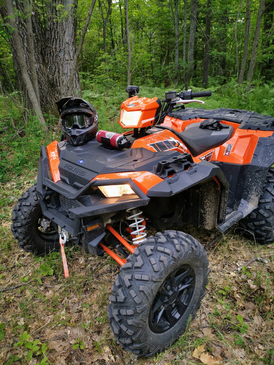 An orange ATV with a helmet on the front, featuring a black universal holder mounted using two screws in a forested area.