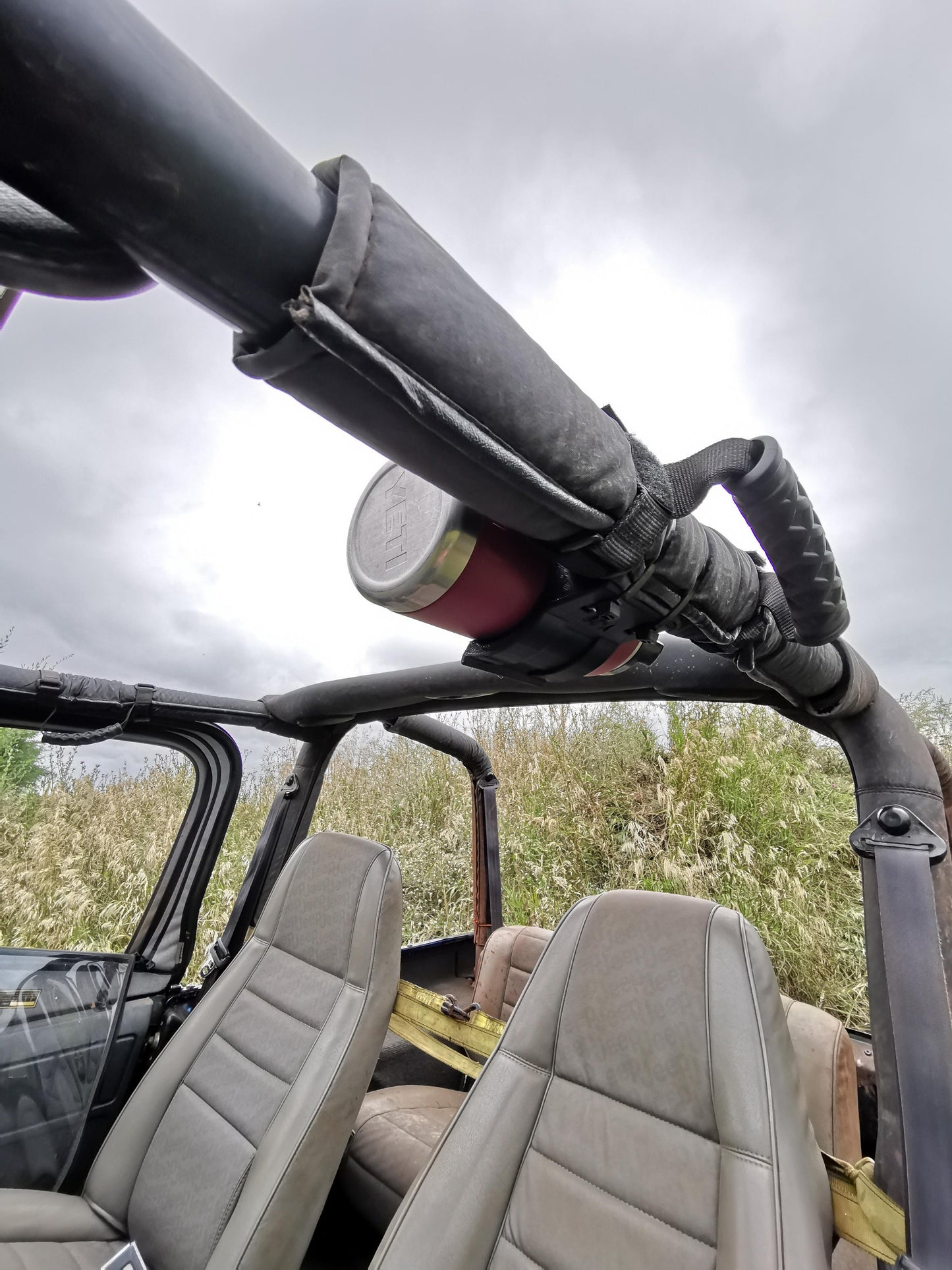 Jeep YJ roll bar with a mounted water bottle holder in the vehicle interior, featuring padded roll bars and front seats for off-road use.