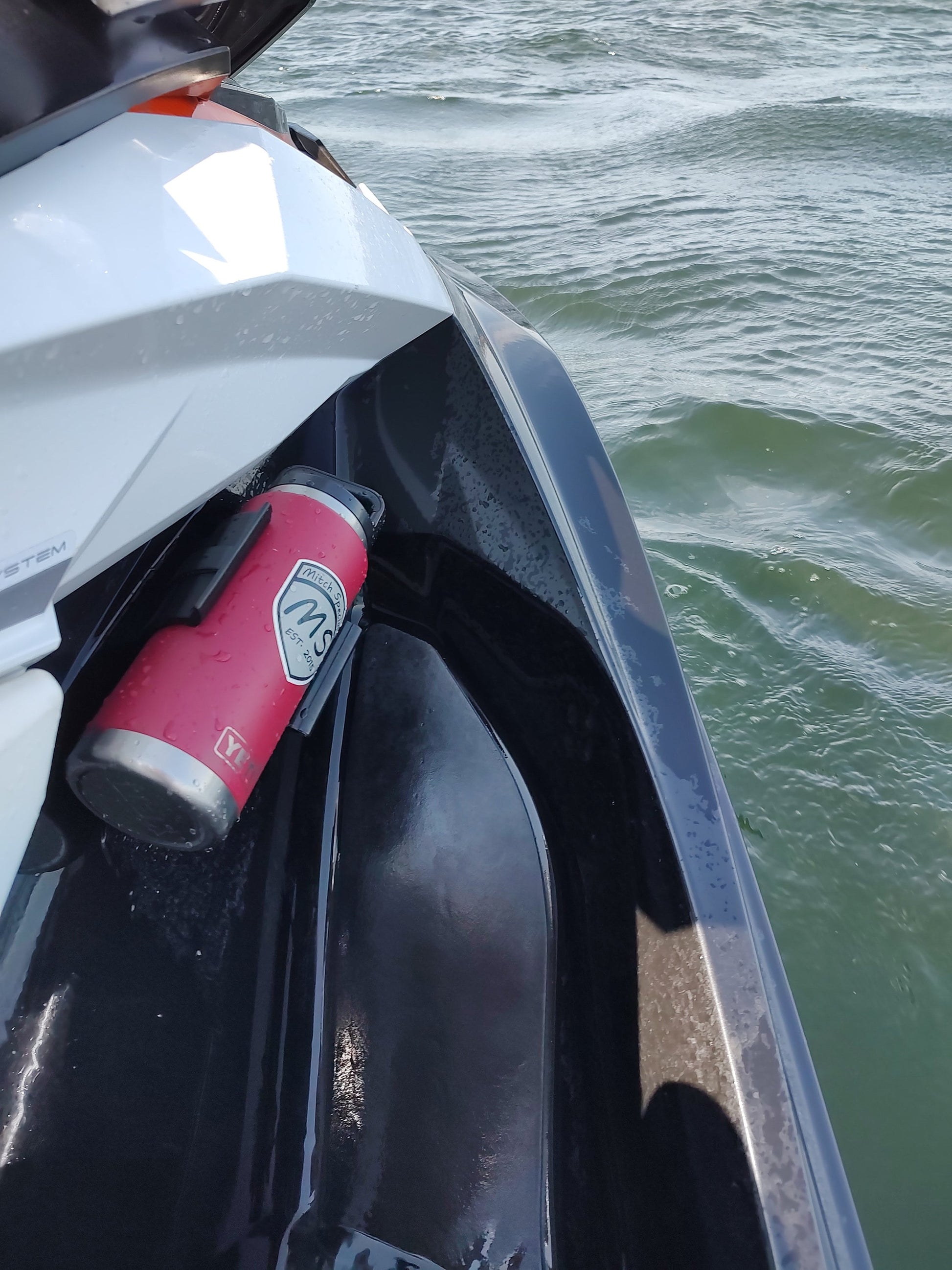 A red bottle holder mounted on a watercraft using 3M VHB tape, securely holding a bottle near the water's edge.