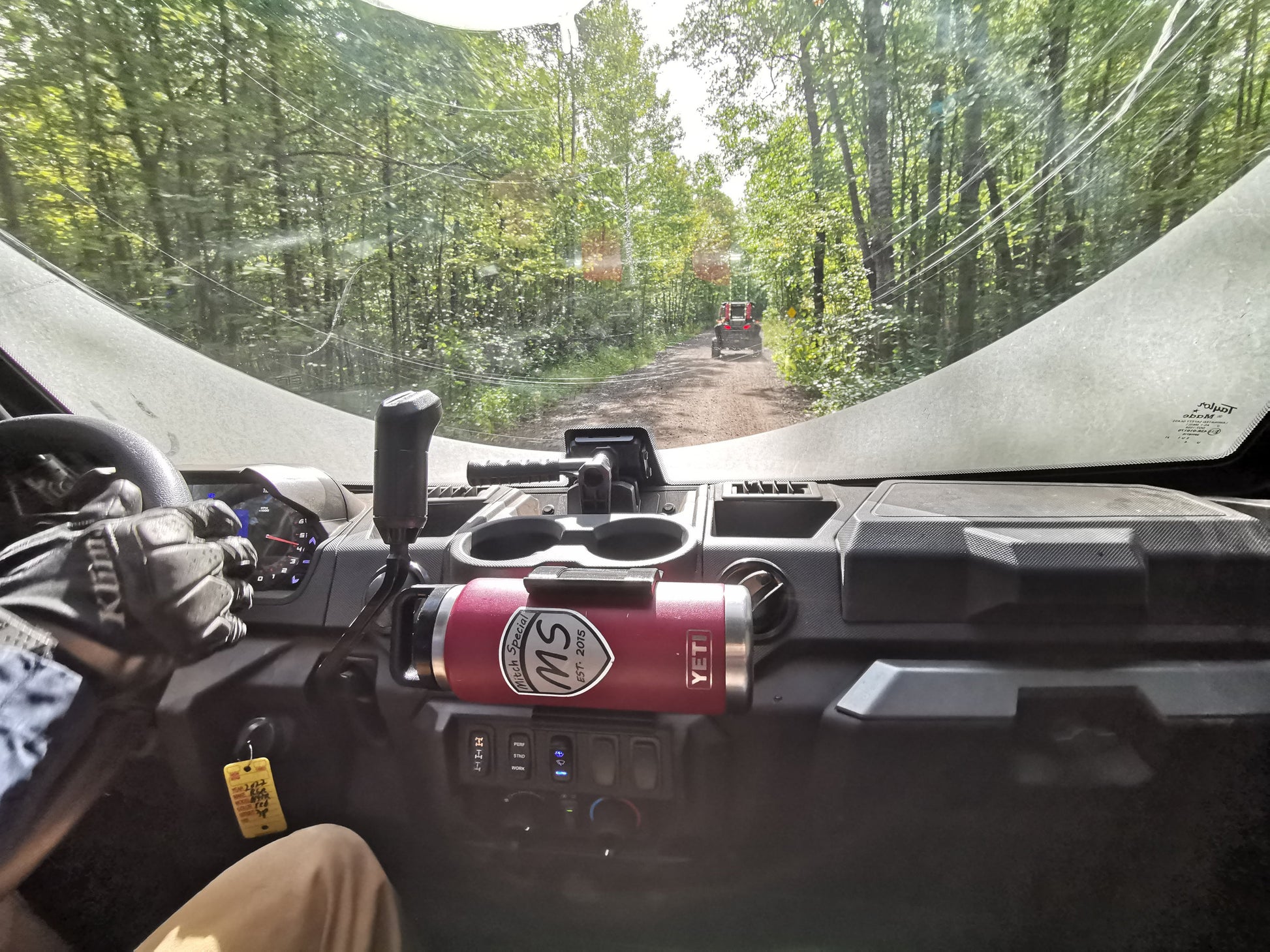 Interior view of a vehicle driving on a forest trail, featuring a universal holder with a red YETI bottle mounted using 3M VHB tape.