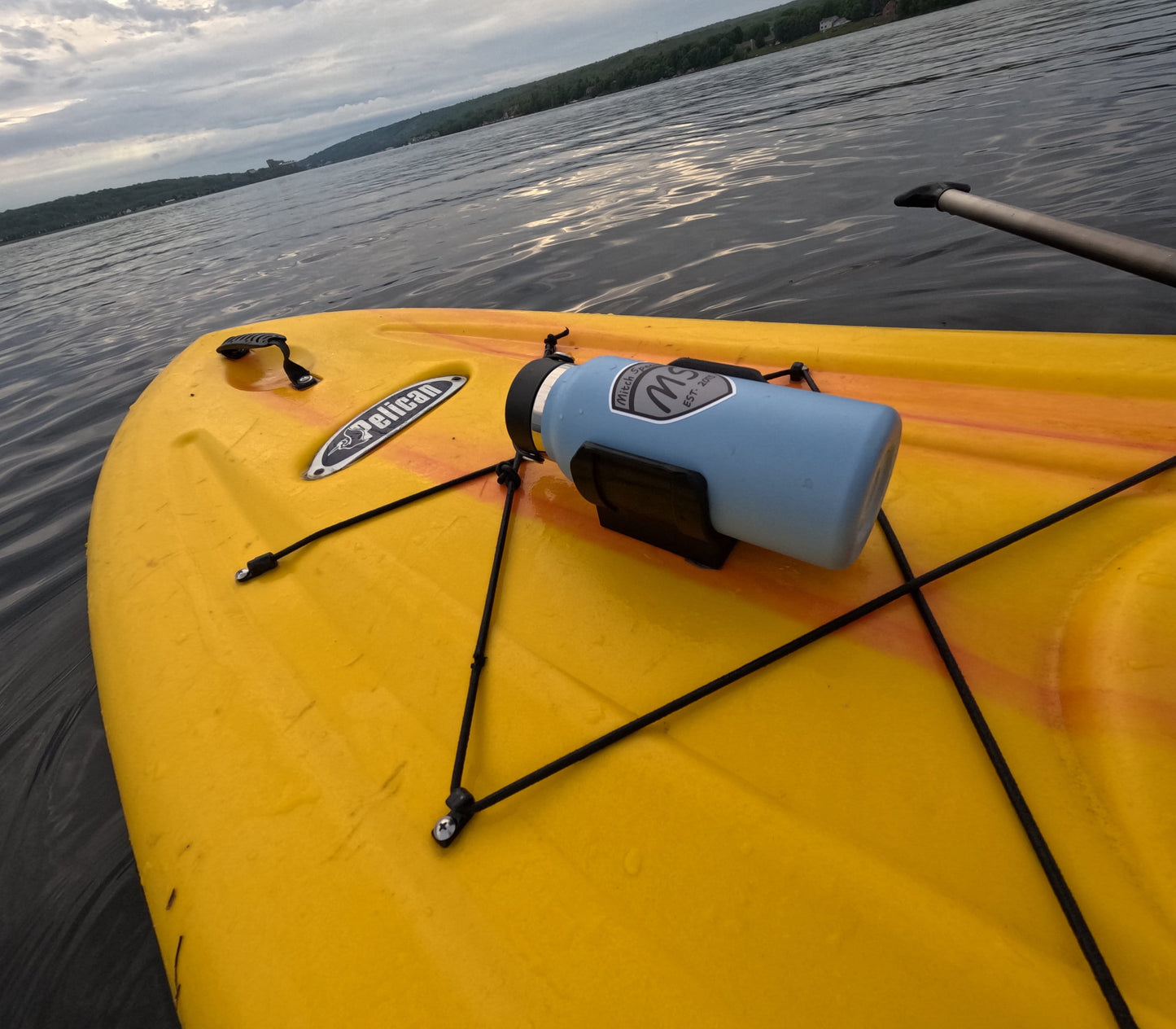 A blue water bottle secured in a universal holder mounted on a yellow kayak using 3M VHB tape, floating on a calm lake.