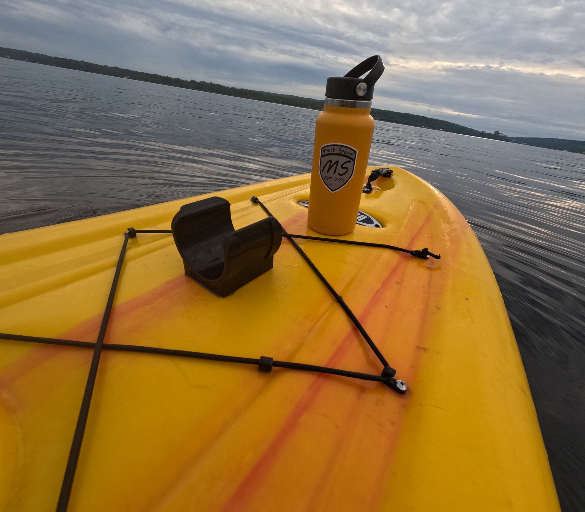 A yellow kayak on a lake with a black universal holder mounted using 3M VHB tape and a yellow water bottle secured on the kayak.
