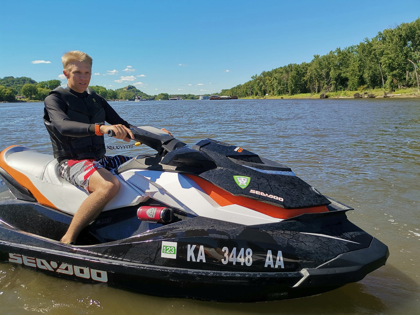 A universal holder mounted on a jet ski using 3M VHB tape, securely holding a red can and a red water bottle on a calm lake.