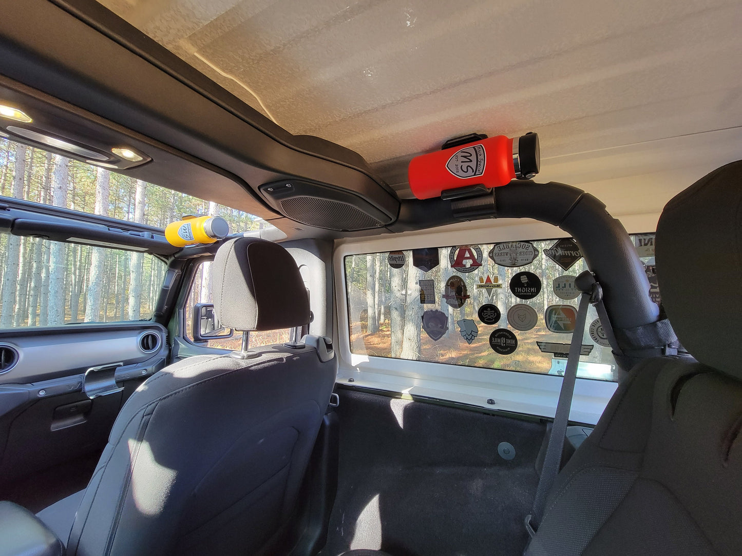 Jeep JL interior with water bottle holder mounted on the roll bar, securing a red and a yellow bottle, ideal for off-road.