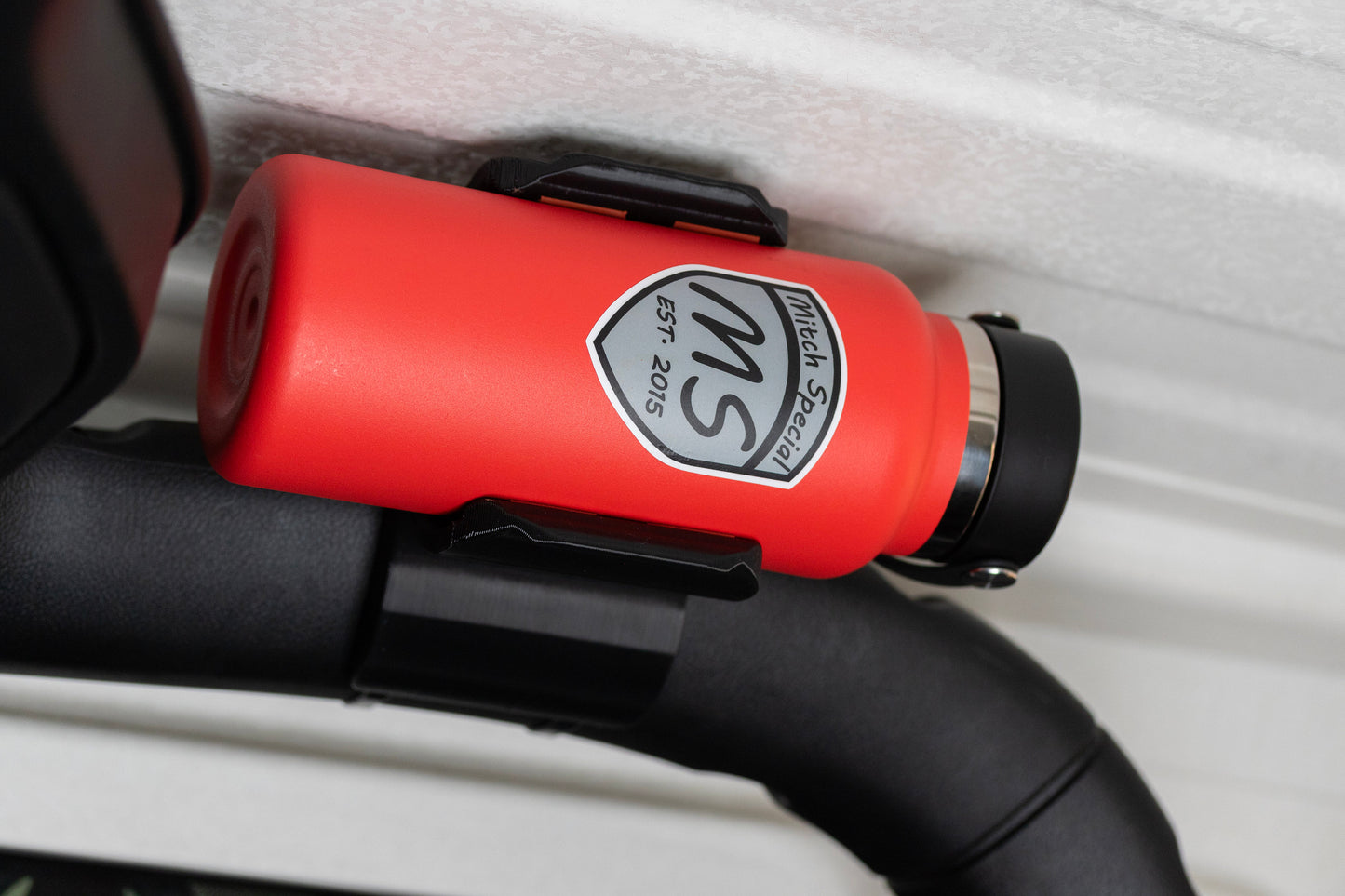 Red water bottle in Jeep JL holder securely mounted on roll bar near the roof, ideal for off-road adventures and ample headroom.