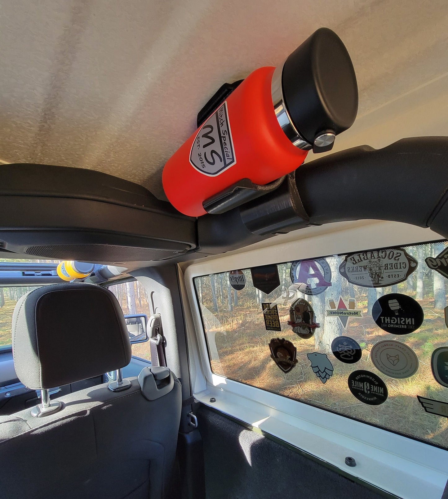 Jeep JL water bottle holder with bright orange silicone inserts for added grip, designed to fit the roll bar contours, holding a red bottle.