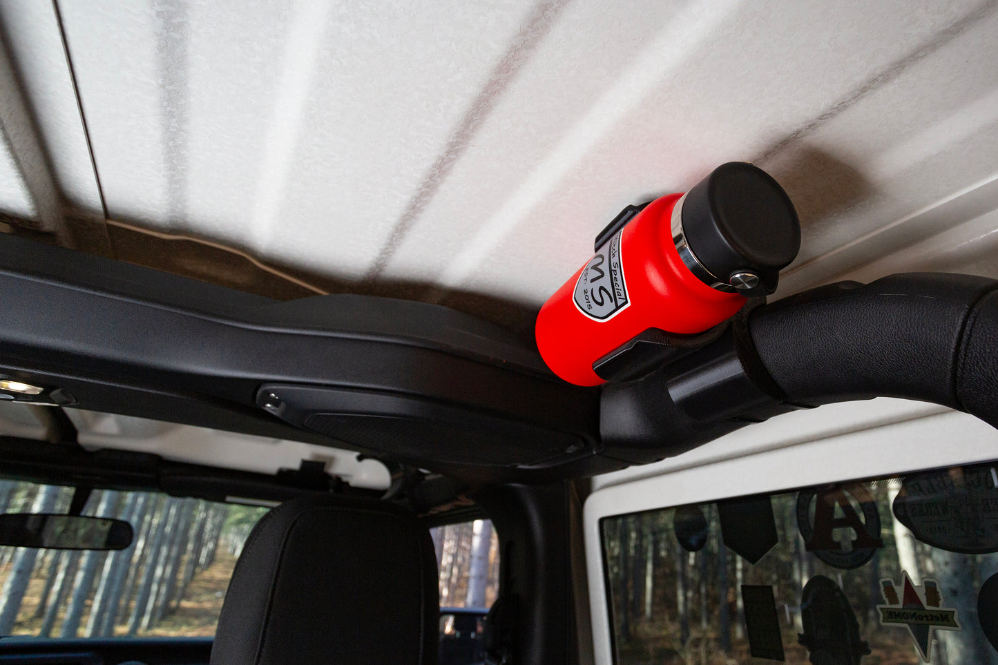 Jeep JL water bottle holder securely mounted on roll bar with red bottle, showcasing practical interior accessory for off-road adventures.