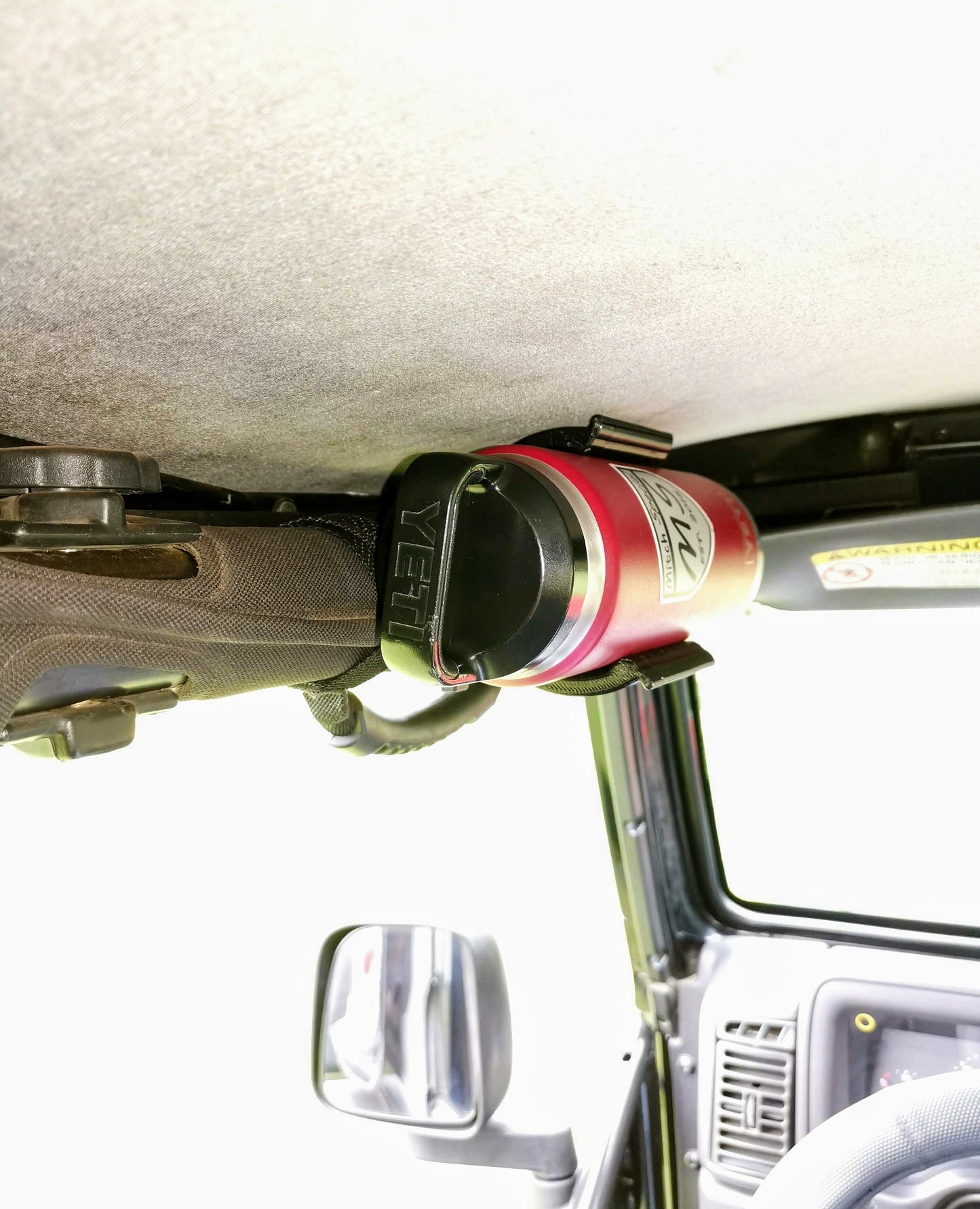 Close-up view of a red YETI water bottle secured in a Mitch Special holder attached to the overhead grab bar inside a Jeep Wrangler, showcasing durable and functional interior accessories.