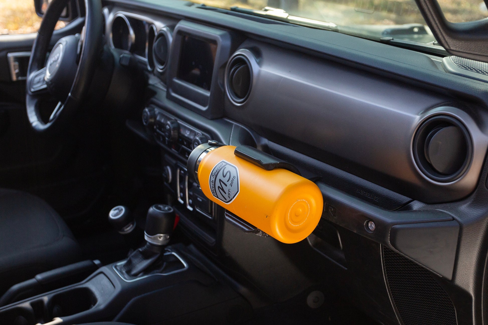 Passenger side view of Jeep JL water bottle holder mounted to grab handle, demonstrating its space-saving design and ergonomic placement, allowing for easy entry and exit without obstruction