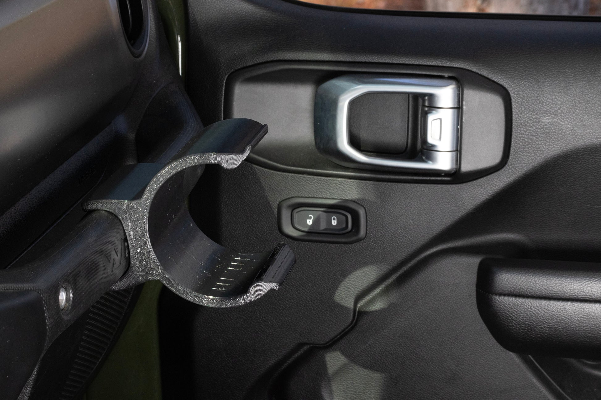 View from driver's seat of Jeep JL interior, featuring empty water bottle holder mounted to grab handle, demonstrating easy reach and visibility, with no obstruction to driver's view or movement