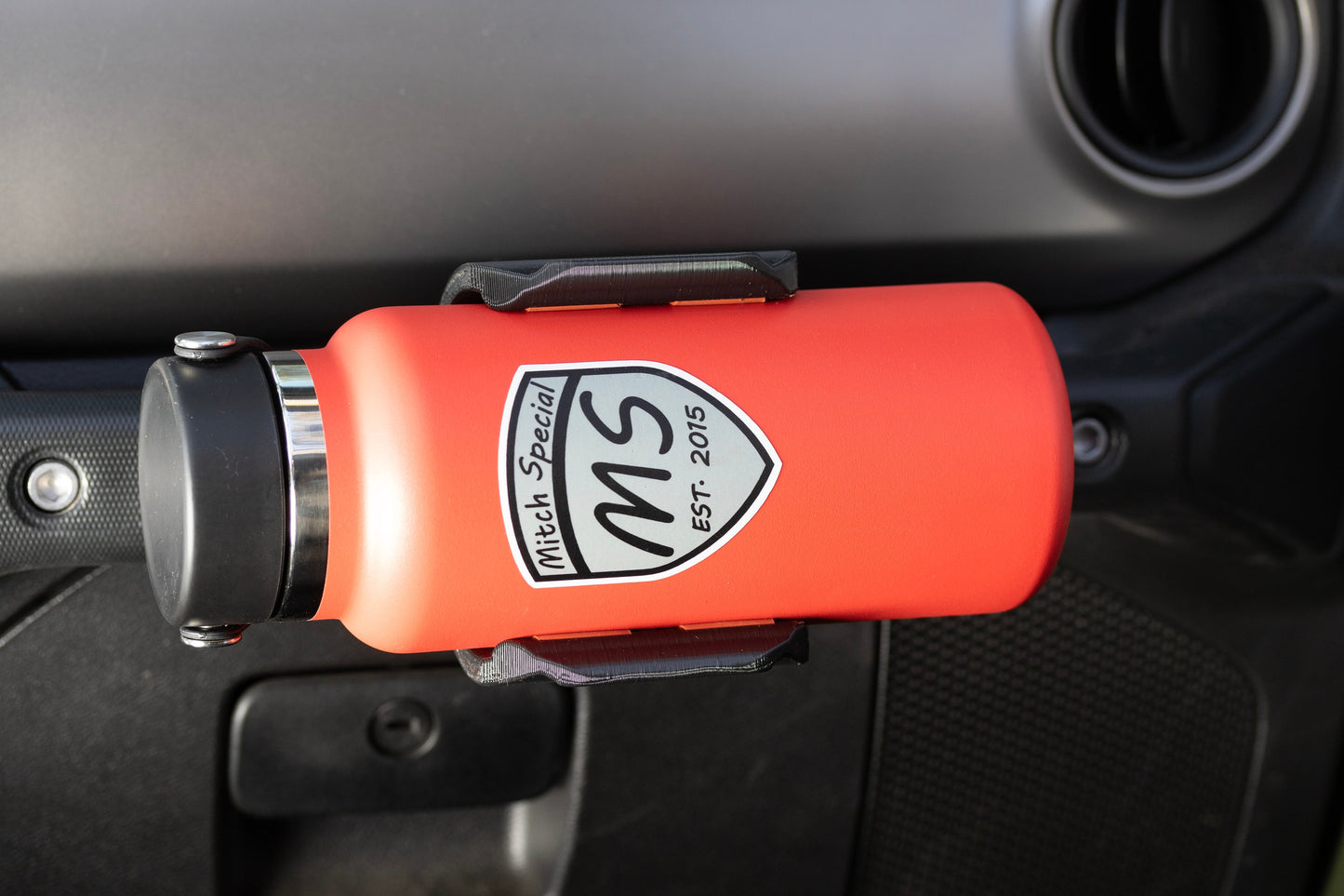 Close-up view of Heavy-Duty Water Bottle Holder for Jeep JL mounted to grab handle from passenger seat perspective, highlighting its sturdy construction and secure water bottle fit