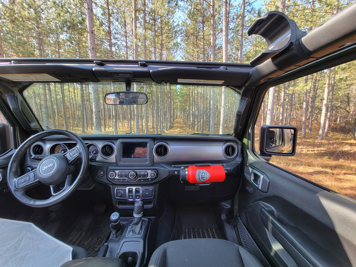 Wide-angle view of Jeep JL interior from passenger seat, featuring Heavy-Duty Water Bottle Holder mounted to grab handle, with roof removed, and roll bar water bottle holder visible in the background, demonstrating the product's seamless integration with the Jeep's design