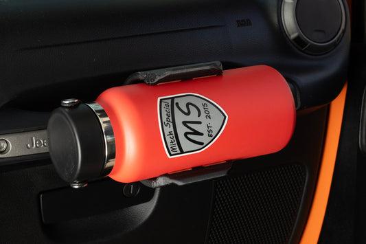 Close-up of a durable red water bottle securely held in a grab handle-mounted holder inside a Jeep Wrangler. Perfect for off-road adventures, this accessory ensures easy access to hydration while maximizing interior space.