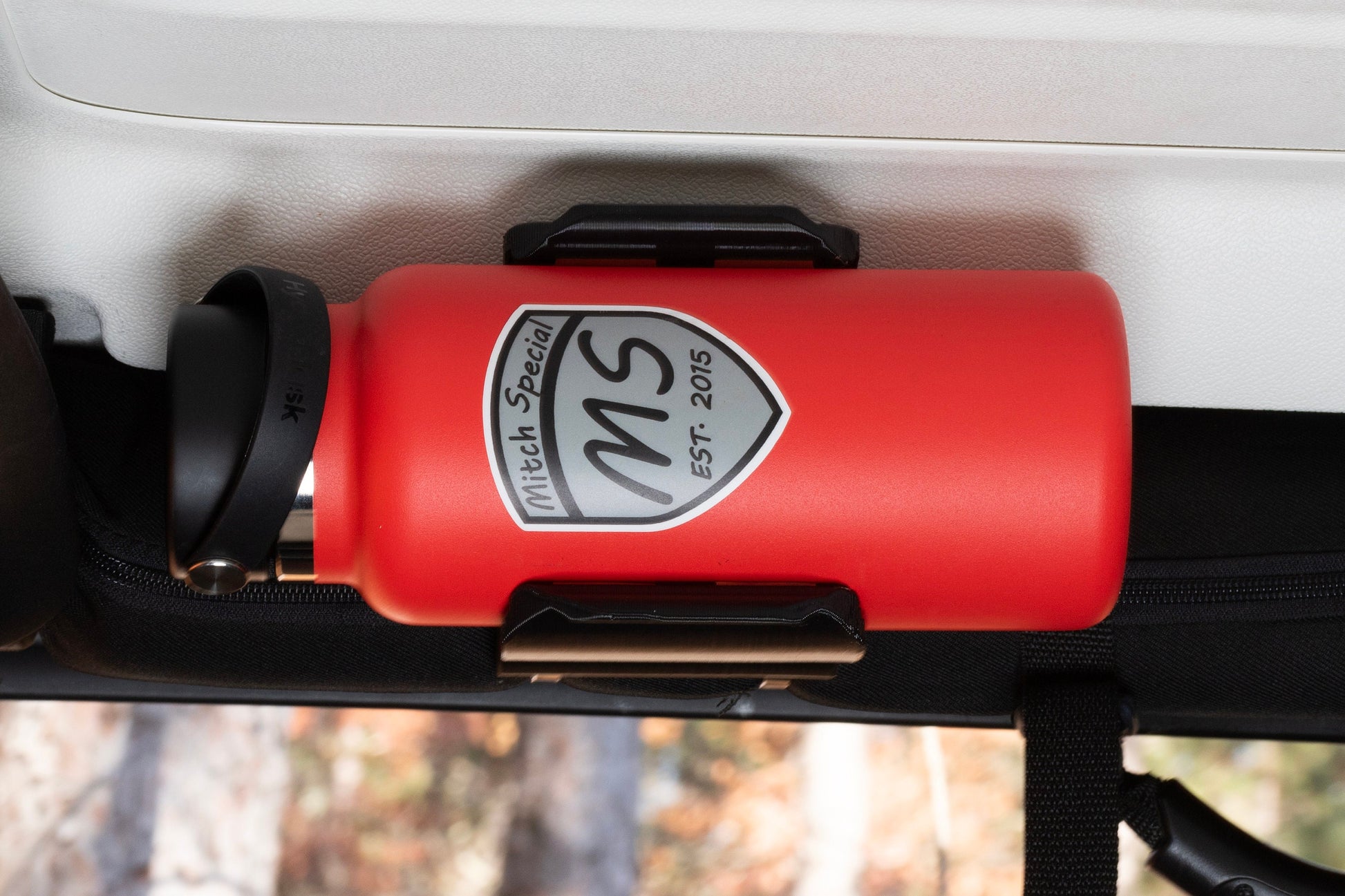 Direct view of Jeep Wrangler JK roll bar water bottle holder, highlighting space-efficient design that fits snugly within door frame, with water bottle fully secured.