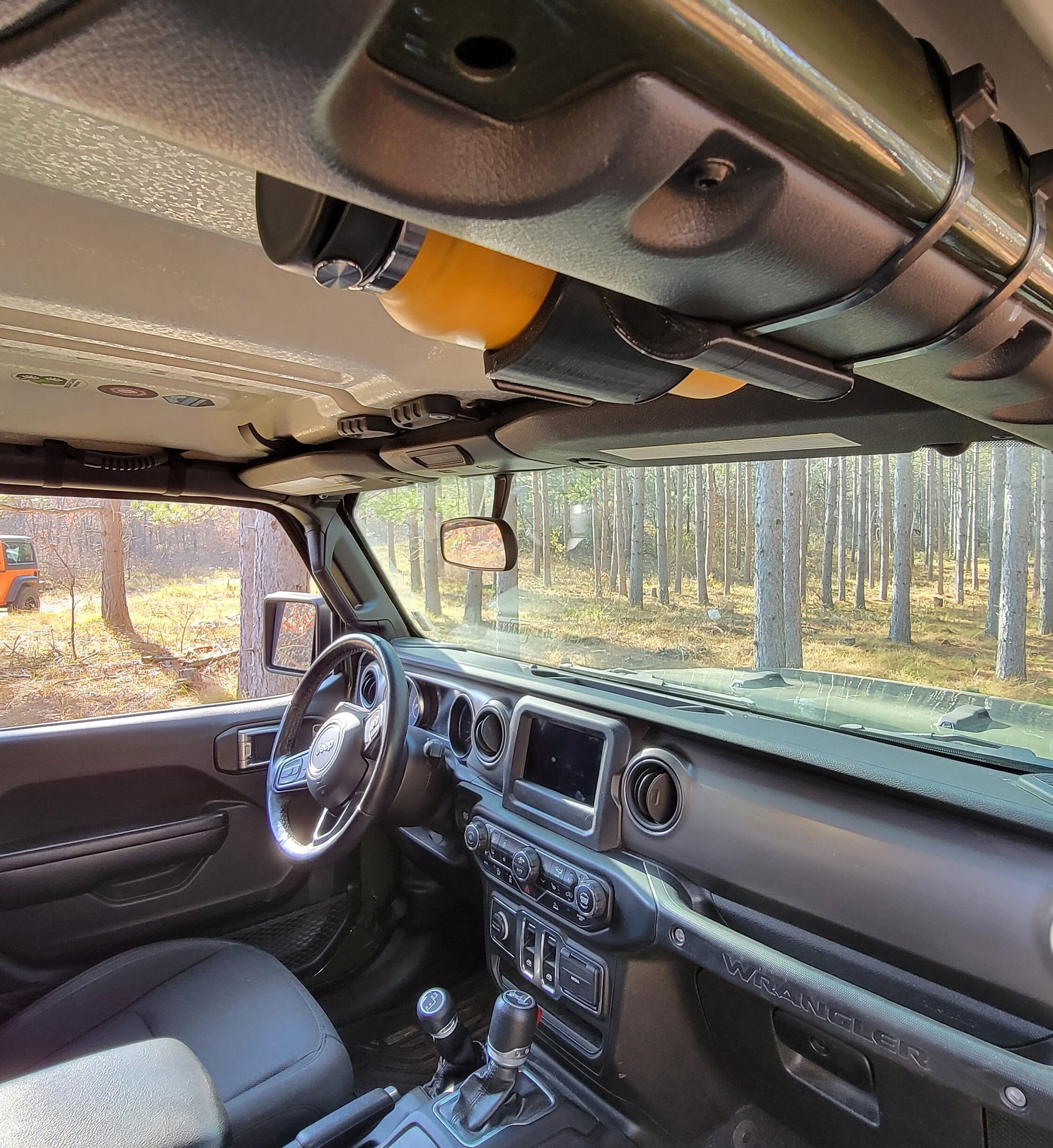 Image of Jeep JL interior, viewed from passenger's entry point, showing a water bottle holder mounted to the front roll bar with two heavy-duty zip ties, securely holding a water bottle in place