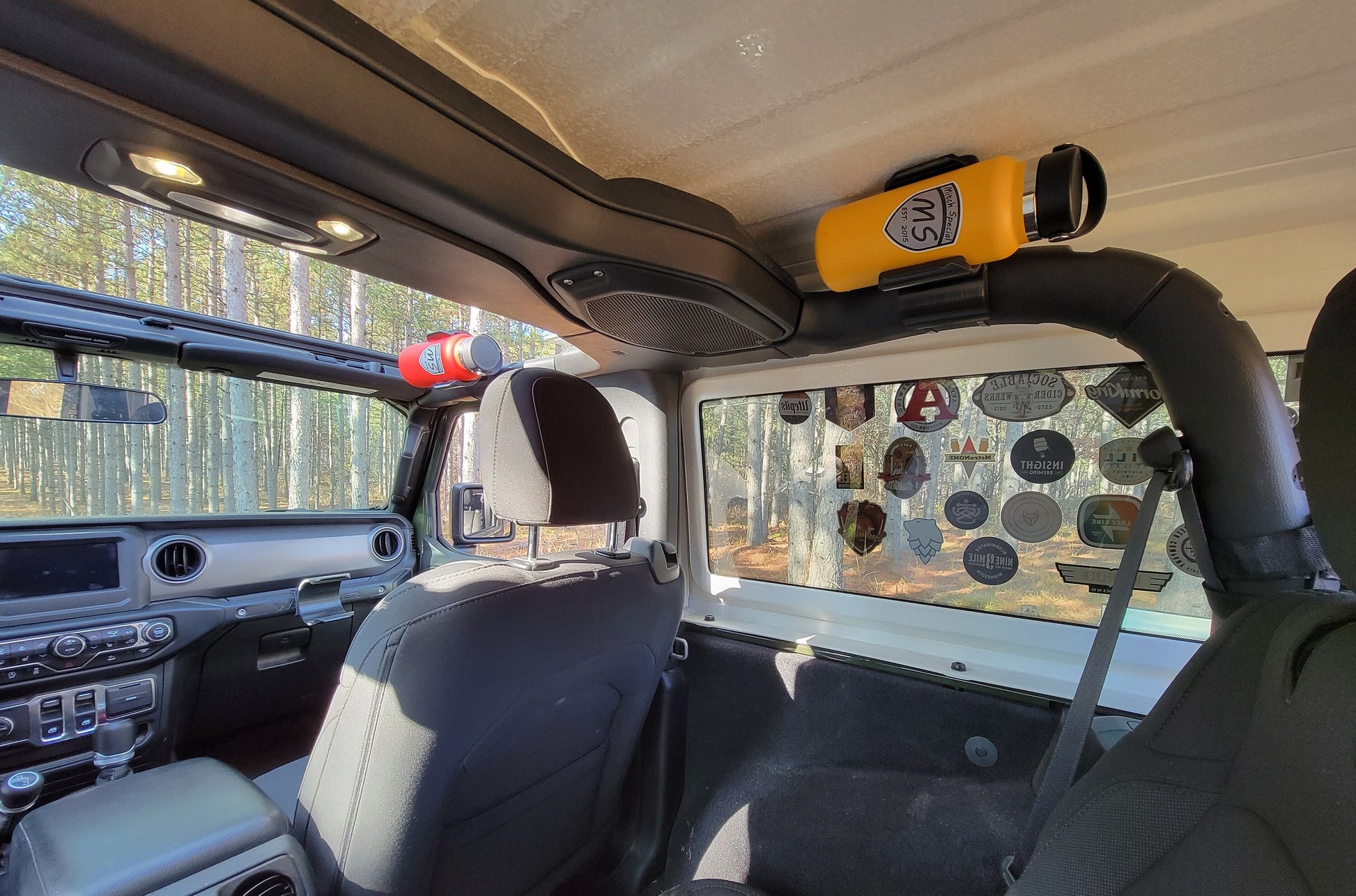 A Jeep JL featuring two water bottle holders mounted on the roll cage. The rear holder is positioned on the back roll bar, while the front holder is attached to the front roll bar, showcasing a practical design for both front and rear seat passengers.