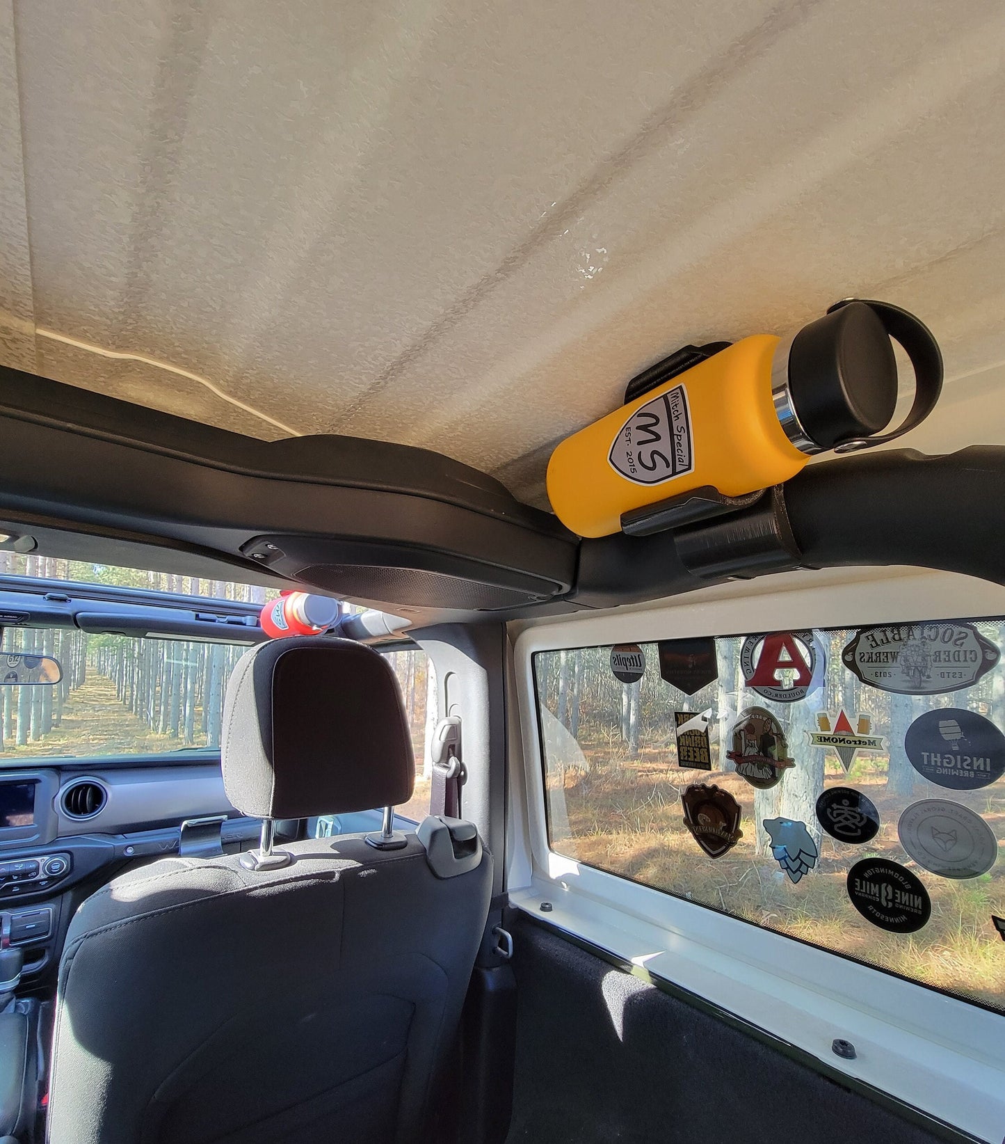 A Jeep JL featuring two water bottle holders mounted on the roll cage. The rear holder is positioned on the back roll bar, while the front holder is attached to the front roll bar, showcasing a practical design for both front and rear seat passengers.