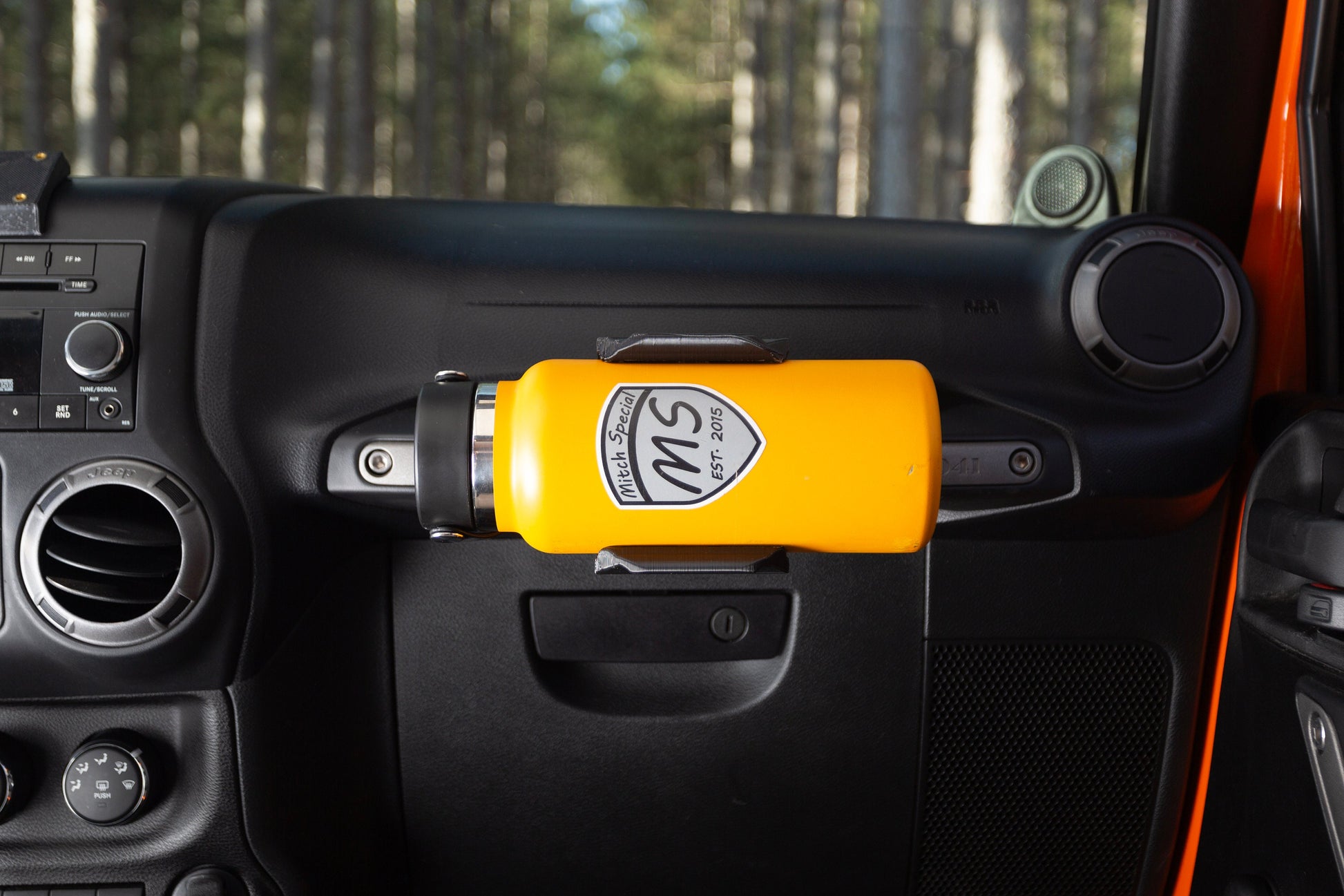 Close-up of a vibrant yellow water bottle securely placed in a holder attached to a Jeep JK passenger grab handle, showcasing a practical and stylish hydration solution for off-road adventures.