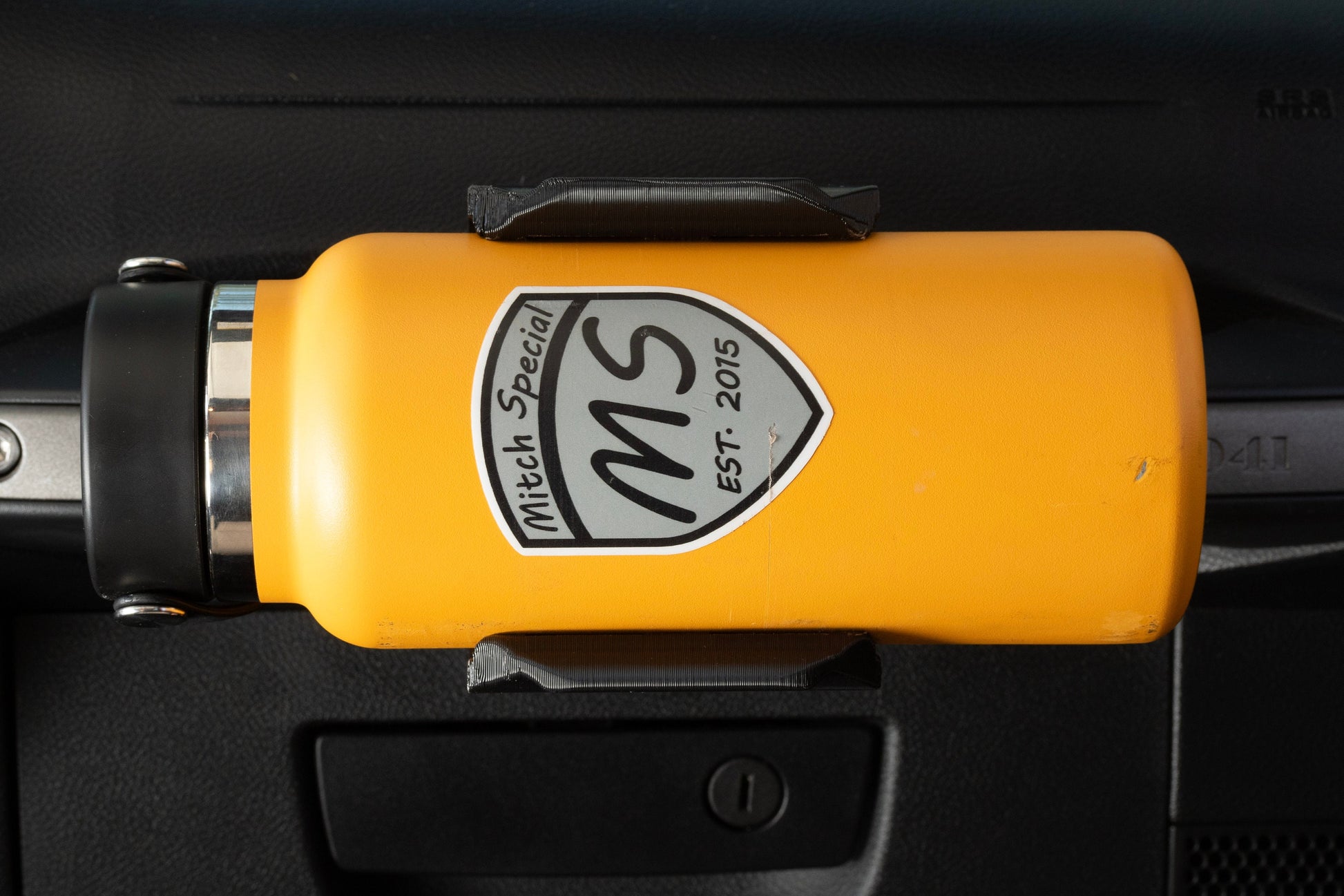 Close-up of a vibrant yellow water bottle securely placed in a holder attached to a Jeep JK passenger grab handle, showcasing a practical and stylish hydration solution for off-road adventures.