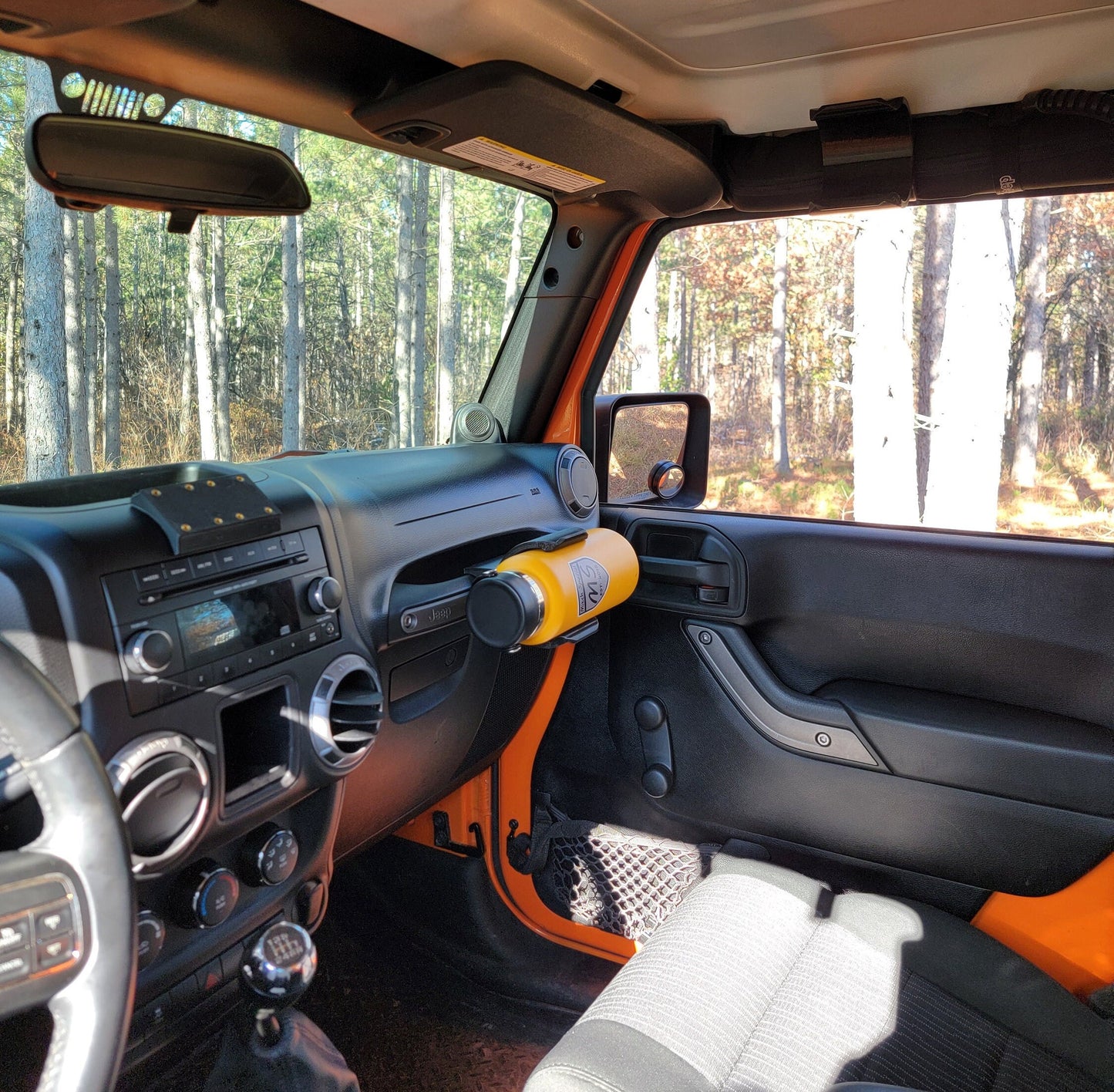 Interior of a Jeep Wrangler with an orange door panel, featuring a yellow water bottle securely held by a grab handle-mounted holder, designed for off-road convenience and accessibility.