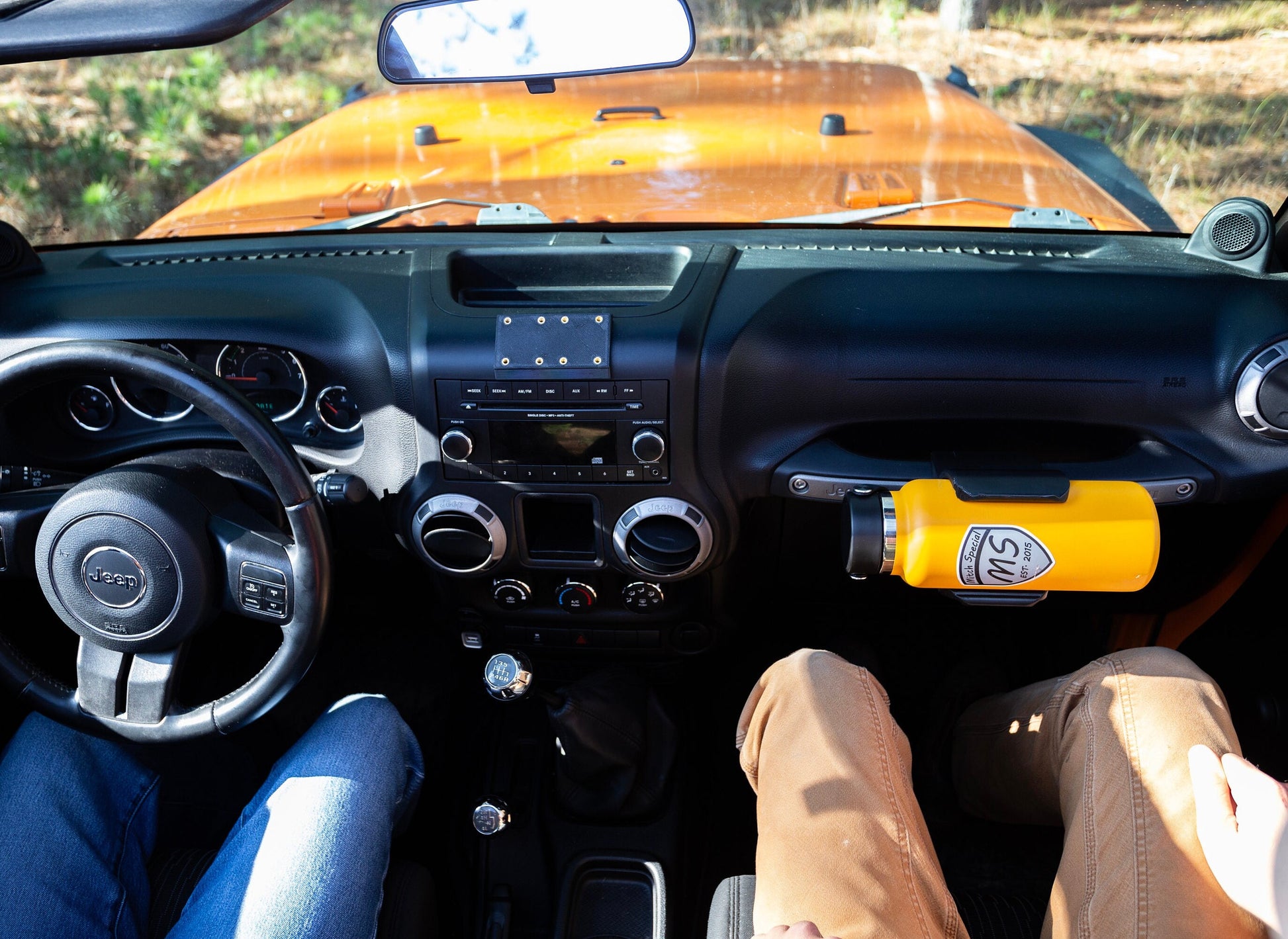 Yellow water bottle mounted in a holder on the passenger grab handle of a Jeep JK, with a view of both the driver and passenger seats, highlighting the spacious interior and convenient design of this Jeep accessory—perfect for off-road enthusiasts.