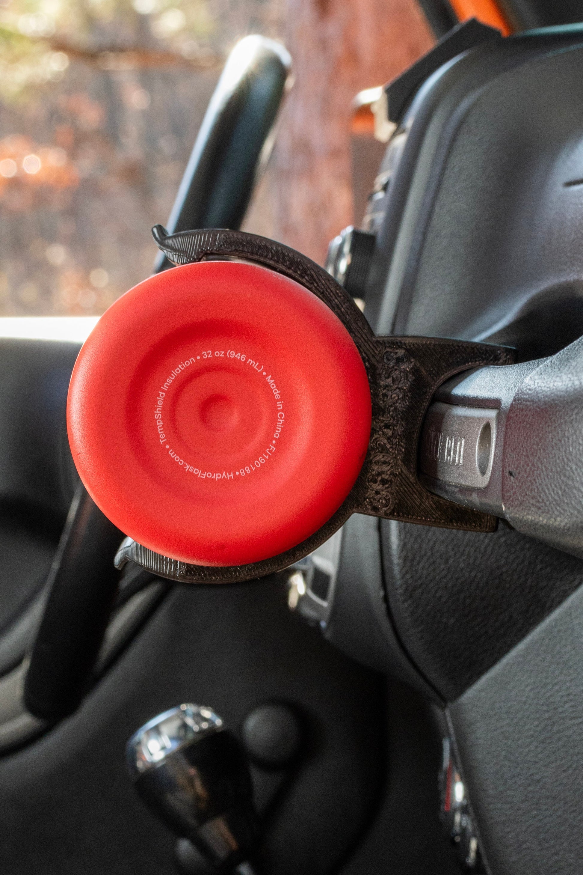 Close-up of a red 32 oz water bottle securely held by a durable water bottle holder attached to a Jeep Wrangler grab handle, highlighting its functional design and compatibility with off-road vehicle interiors.