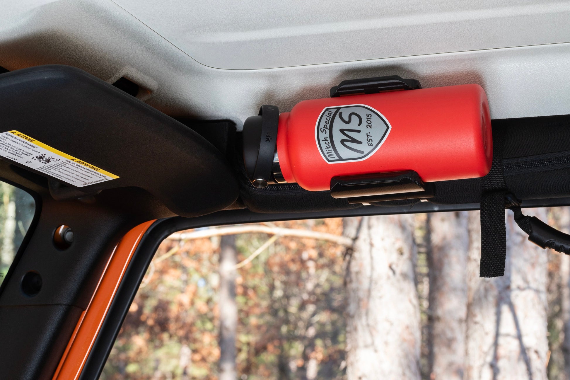 Straight-on view of Heavy-Duty Water Bottle Holder installed on Jeep Wrangler roll bar, showcasing slim design that doesn't obstruct door opening, with water bottle securely in place.